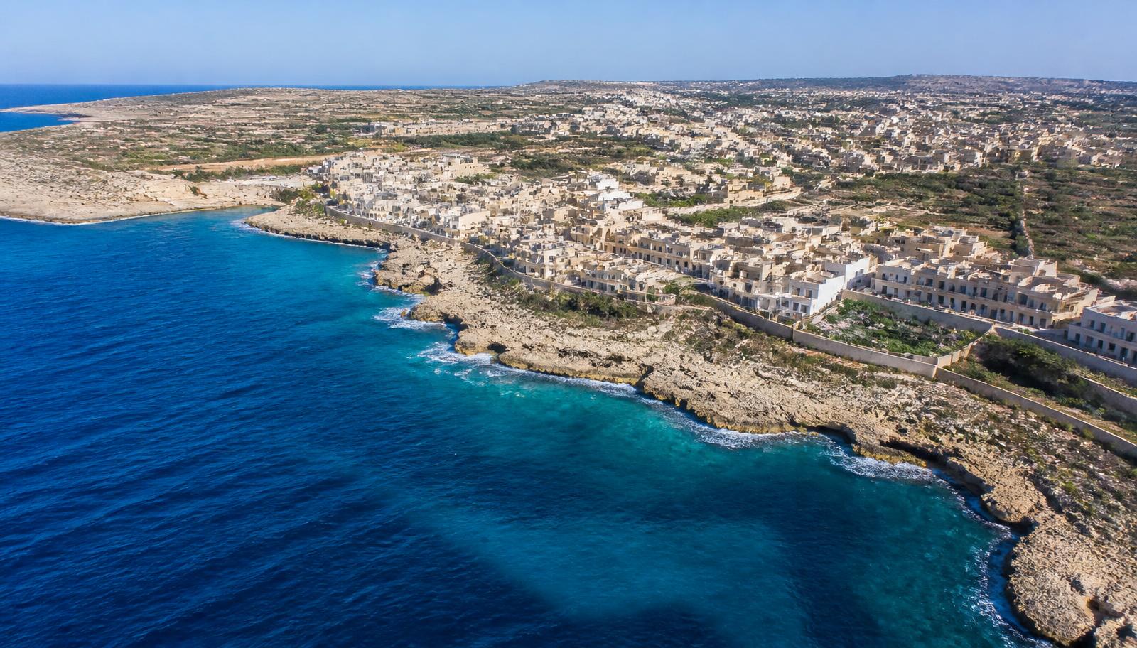Luchtfoto van de Maltese kust met rotsachtige kliffen, helderblauw water en een dorp met kalkstenen huizen
