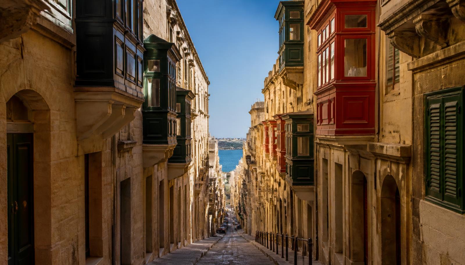 Smalle straat in Valletta met kalkstenen gevels, traditionele houten erkers en uitzicht op de zee