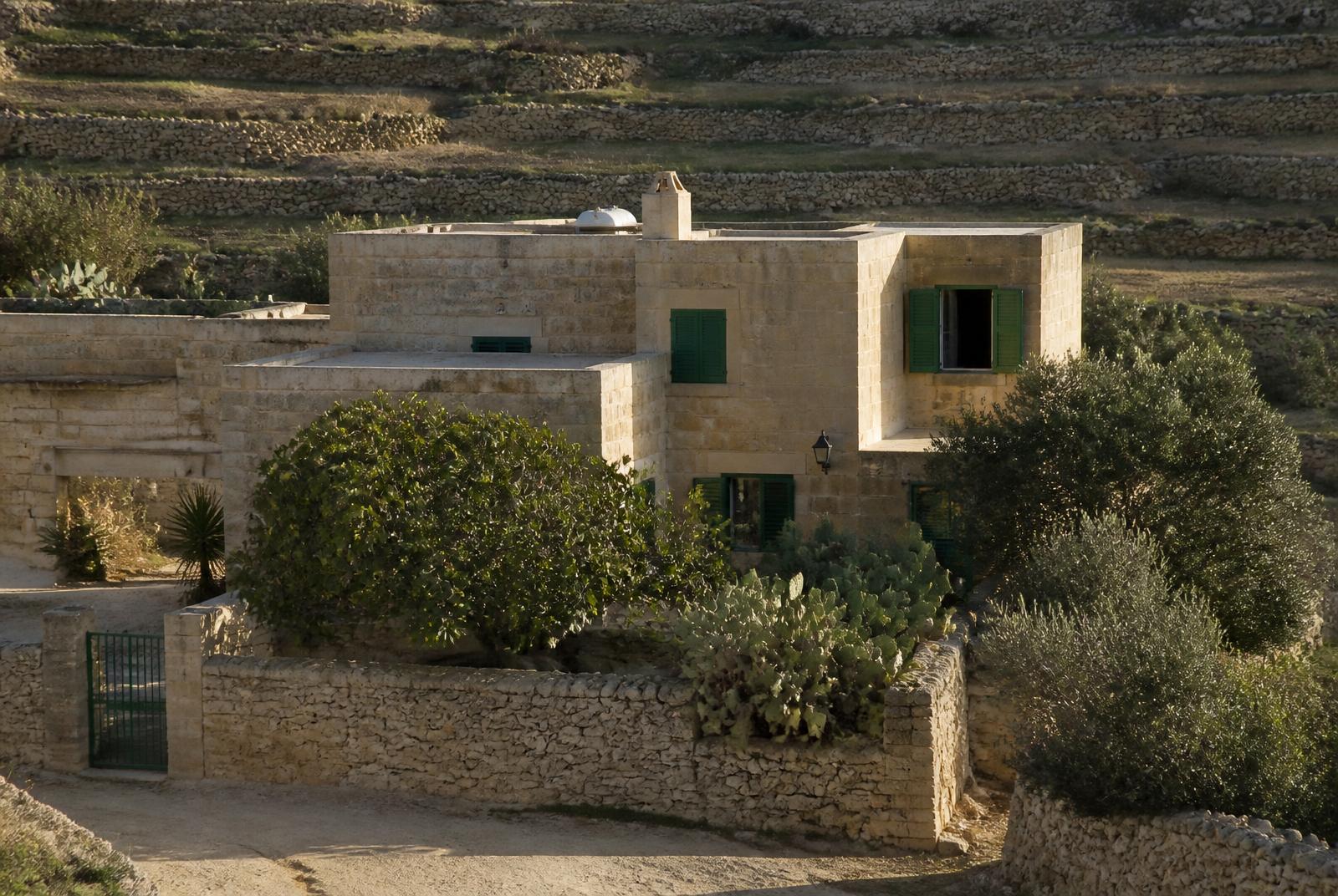 Traditionele Gozitaanse kalkstenen woning met groene luiken, binnenplaats en droge stenen muren tussen terrasvelden op Gozo