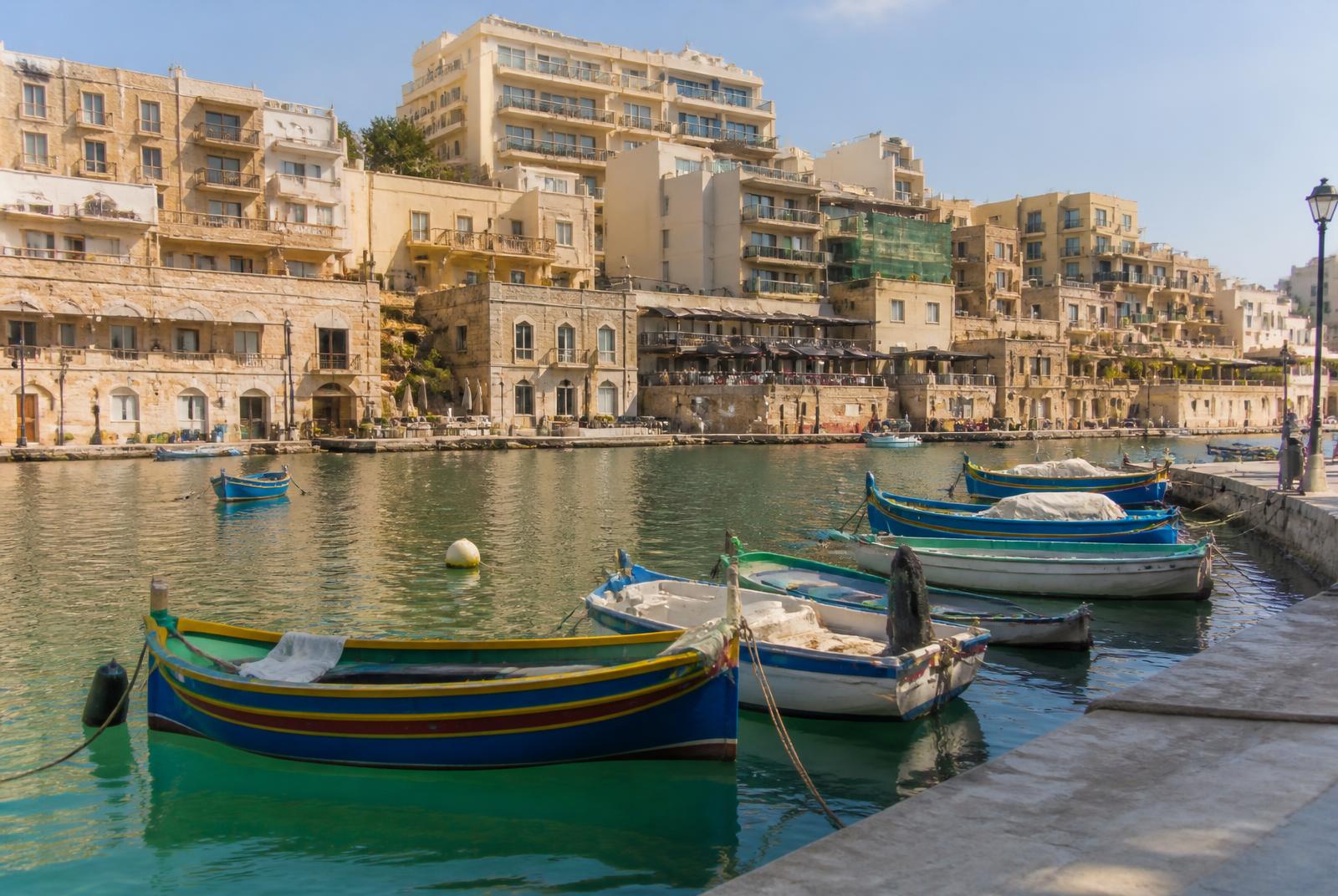Traditionele gekleurde vissersboten in Spinola Bay in St. Julian's met kalkstenen huizen en terrassen langs de baai